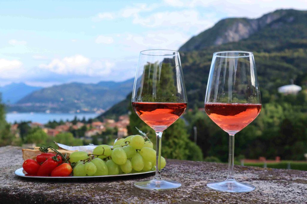 Par de copas de vino rosado y al lado un plato con uvas sobre una mesa con vista a las montañas y el lago