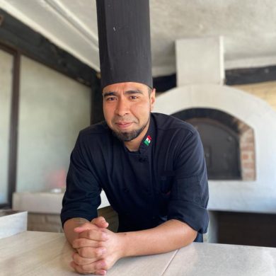Chef joven frene a un horno de leña con filipina y gorra negra